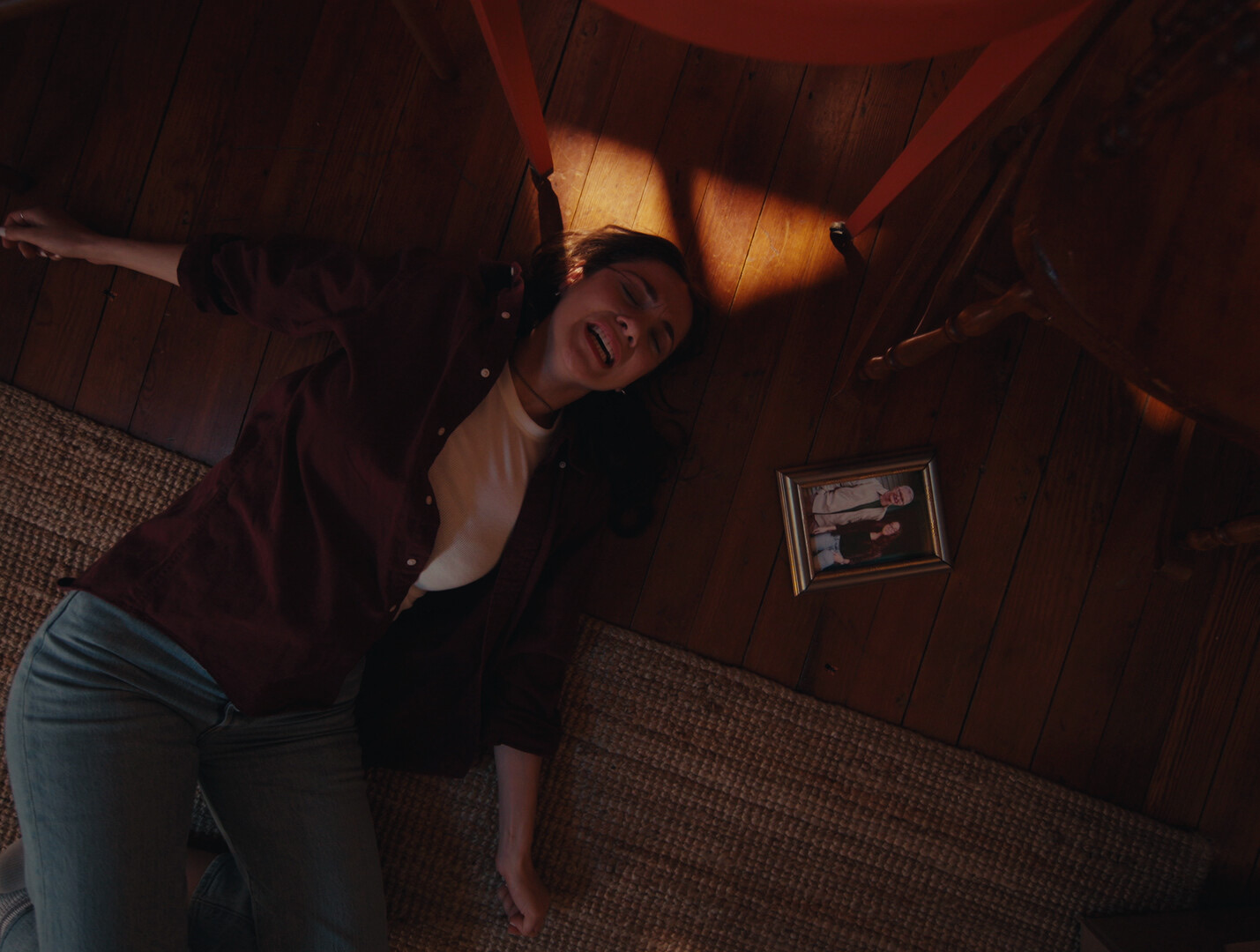 Still from The Flies: a woman lying on the floor beside a framed photo of her father